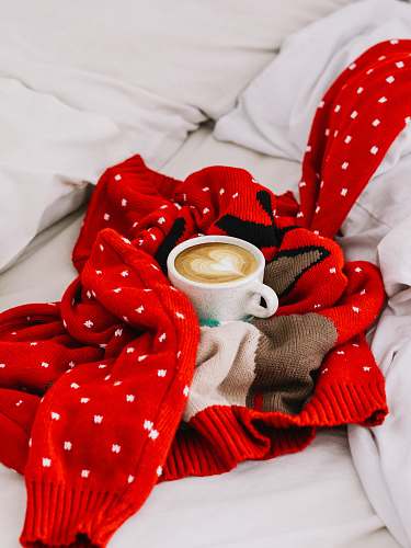 coffee cup round white ceramic mug with coffee beverage inside on top of red and white polka dot knitted sweater apparel